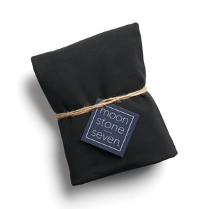 A black hair plop, which is cut fabric folded into a rectangle and tied with a piece of thin twine with a navy blue MoonstoneSeven product tag in the middle.