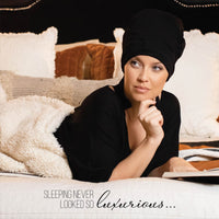 Model wearing MoonstoneSeven Satin Sleeper in bed while reading, showing comfortable nighttime curl protection