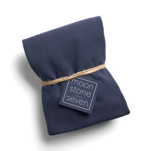 A navy hair plop, which is cut fabric folded into a rectangle and tied with a piece of thin twine with a navy blue MoonstoneSeven product tag in the middle.  Edit alt text